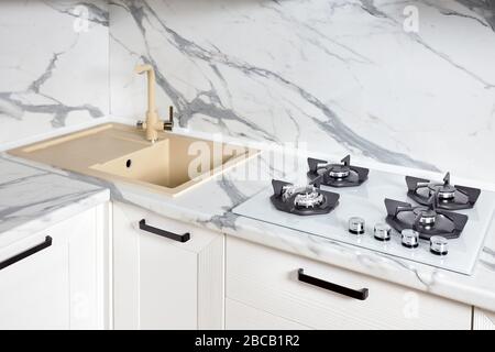 Modernes Design mit Chrom-Wasserhahn über Edelstahlwaschbecken auf der Tischplatte aus weißem Steinmarmor oder Granit. Stockfoto