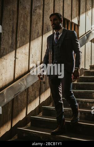 Ernst trendy Geschäftsmann mit Sonnenbrille und zu Fuß die dunkle Treppe mit Sonnenlicht hinter ihm Stockfoto