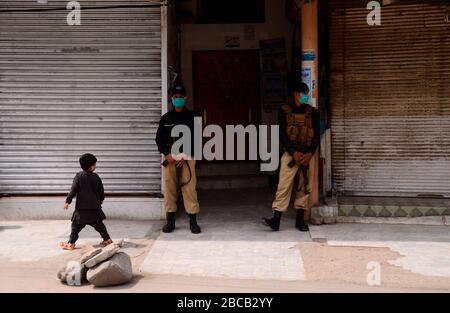 April 2020: Peschawar, Pakistan. März 2020. Die Menschen gehen in einer Straße entlang eines stillgelegten Marktes, der von Polizeibeamten in der nordpakistanischen Stadt Peschawar bewacht wird. Die Märkte bleiben in Peschawar im Rahmen von Vorsichtsmaßnahmen geschlossen, um die Ausbreitung von Covid-19 im Land zu vermeiden Credit: Hasnain Ali/IMAGESLIVE/ZUMA Wire/Alamy Live News Stockfoto