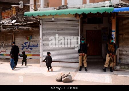 April 2020: Peschawar, Pakistan. März 2020. Die Menschen gehen in einer Straße entlang eines stillgelegten Marktes, der von Polizeibeamten in der nordpakistanischen Stadt Peschawar bewacht wird. Die Märkte bleiben in Peschawar im Rahmen von Vorsichtsmaßnahmen geschlossen, um die Ausbreitung von Covid-19 im Land zu vermeiden Credit: Hasnain Ali/IMAGESLIVE/ZUMA Wire/Alamy Live News Stockfoto