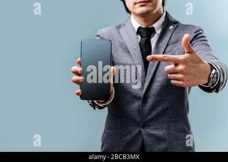 Der junge Mann hält das Telefon in der Hand und zeigt mit dem Finger auf dem Bildschirm Stockfoto