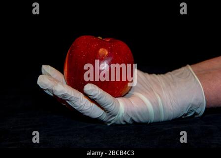 Die Hand einer älteren Frau in Gummihandschuhen hält einen roten Apfel. Stockfoto