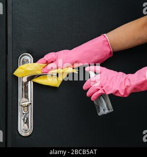 Hände in rosafarbenen Handschuhen, die Metallgriff an einer Eingangstür reinigen Stockfoto