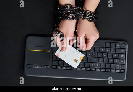 Frau mit Metallkette, die Kreditkarte über Tastatur hält, Online-Shopping-Suchtkonzept Stockfoto