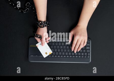 Frau mit Metallkette, die Kreditkarte über Tastatur hält, Online-Shopping-Suchtkonzept Stockfoto