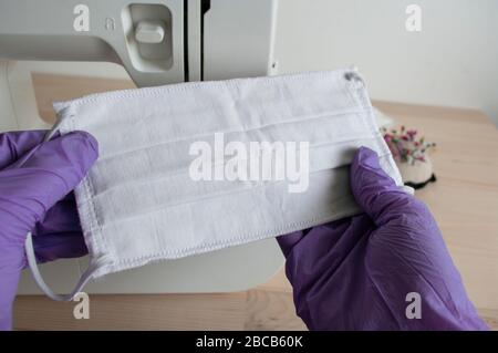 Hände in violetten Handschuhen mit Maske. Maschine hinten nähen.Schützen Sie sich vor Coronavirus, Nähen medizinische Gesichtsmaske zu Hause. Stockfoto