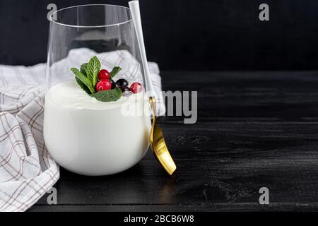 Hausgemachter Joghurt in einem hohen Glas auf dunklem Hintergrund. Garniert mit Minze und Preiselbeeren. Gesunde Ernährung. Vegetarisches Essen. Kopierbereich Stockfoto