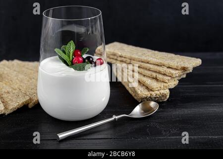 Hausgemachter Joghurt in einem hohen Glas auf dunklem Hintergrund. Garniert mit Minze und Preiselbeeren. Gesunde Ernährung. Vegetarisches Essen. Kopierbereich Stockfoto