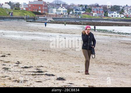 April 2020 EINE junge Frau auf einem Handy, während sie während der Covid 19 Viru an der Wasserlinie am Strand von Ballyholme in Bangor Nordirland spazieren ging Stockfoto
