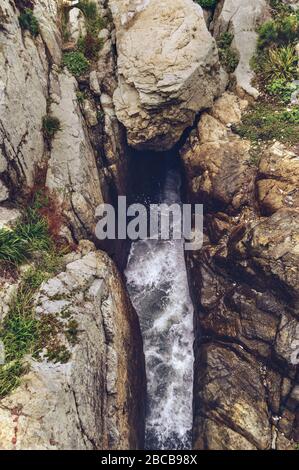 Blick von oben auf den schmalen natürlichen Kanal in massiven Felsen mit heftigen Wasserwellen vom nahe gelegenen Meer Stockfoto