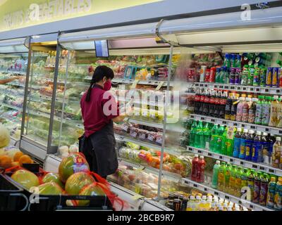 SINGAPUR - 2. APR 2020 - maskenbekleideten Supermarktmitarbeiter kleben Etiketten auf Obst und Gemüse in einem NTUC FairPrice Supermarkt Stockfoto
