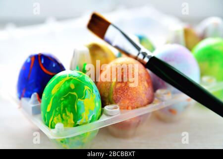 Farbige Eier in einer transparenten Box und einem Kunstpinsel, ein verschwommener Hintergrund, ein hintergrundbeleuchtetes helles Licht Stockfoto