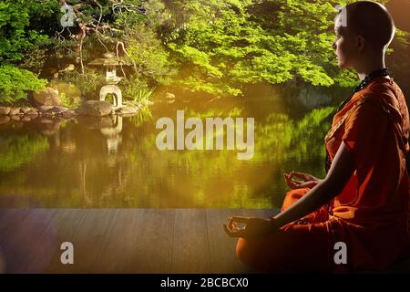 Schöne junge Frau in orange Robe sitzt in Meditation im Garten auf Holzboden..Meditation ist der beste Weg, um das komplexeste Problem zu lösen. Stockfoto