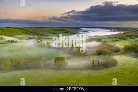 Üppiges grünes Flusstal, gesäumt von Bäumen im Morgennebel in der Toskana, Italien, April. Stockfoto