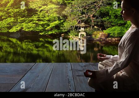 Schöne junge Frau in weißem Gewand sitzt in Meditation im Zen-Garten auf Holzboden...Meditation ist der beste Weg, um das komplexeste Problem zu lösen. Stockfoto