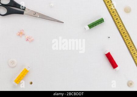 Schere, Maßband, Knöpfe, Spulen mit unterschiedlicher Fadenfarbe zum Nähen auf weißem Grund aus Stoff. Set für Handarbeit Draufsicht Stockfoto