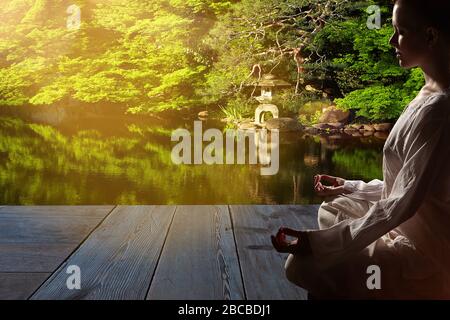 Schöne junge Frau in weißem Gewand sitzt in Meditation im Zen-Garten auf Holzboden...Meditation ist der beste Weg, um das komplexeste Problem zu lösen. Stockfoto