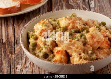 Hähnchenfilet mit grünen Erbsen, die in einer cremigen Soße auf einem Holztisch gedünstet sind Stockfoto
