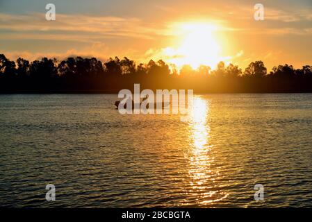 Sonnenaufgang auf dem Fluss. Ein Boot mit Anglern. Schöne Reflexe auf dem Wasser. Stockfoto