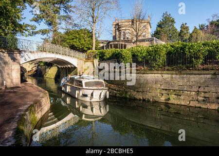 Ein Lastkahn fährt unter einer eisernen Fußgängerbrücke über den Kennet und Avon Kanal in Sydney Gardens, Bath, Somerset England Stockfoto