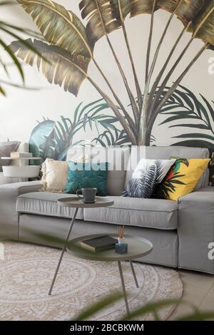 Kleines graues Sofa vor floraler Tapete. Stockfoto