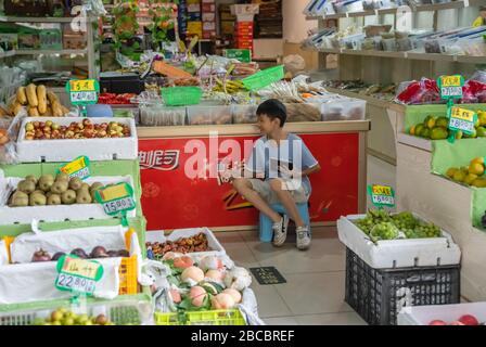 Zigong, China - Juli 2019: Junger Junge, der seiner Mutter hilft und die Produkte im chinesischen Supermarkt Zigong in der Provinz Sichuan sucht Stockfoto