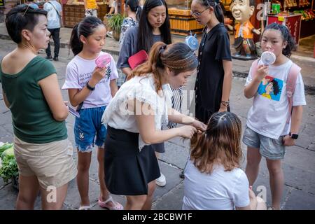 Chongqing, China - August 2019: Frau, die Freunde auf dem Stret in der Altstadt von CI Qi Kou frisiert Stockfoto