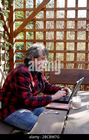 Mann mittleren Alters arbeitet im Heimbüro im Hinterhof-Frühlingsgarten Stockfoto