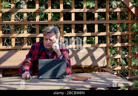 Mann mittleren Alters arbeitet im Heimbüro im Hinterhof-Frühlingsgarten Stockfoto