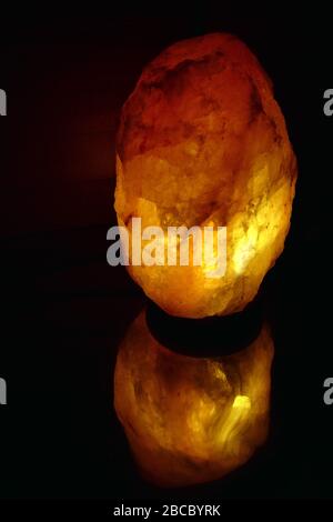 Himalaya-Steinsalzlampe mit eigener Spiegelung auf dunklem Hintergrund Stockfoto