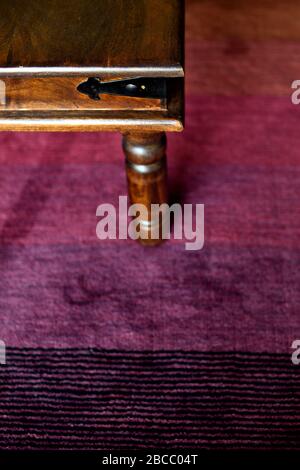 Ecke des Kaffeetabels und des Beins im Fokus auf rotem Teppich Stockfoto