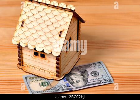 Ein kleines Holzhaus-Sparschwein und eine Banknote 100 Dollar auf einem hölzernen Hintergrund Stockfoto