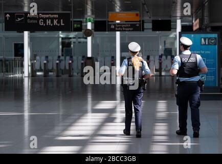 München, Deutschland. April 2020. Zwei Polizisten laufen durch das ansonsten fast menschenleere Terminal des Flughafens München. Durch die Corona-Pandemie ist der Flugverkehr praktisch zum Erliegen gekommen. Credit: Sven Hoppe / dpa / Alamy Live News Stockfoto