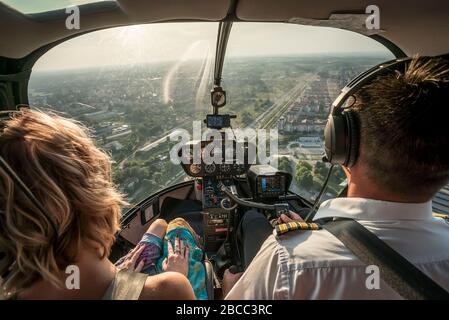 Porträt von schönen blonden Frauen und Piloten genießen Hubschrauberflug. Sie ist begeistert von der Stadtlandschaft und trägt Pilot-Kopfhörer. Stockfoto