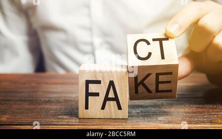 Ein Mann stellt Holzblöcke mit den Worten Fakt und Fake. Konzept von Nachrichten und falschen Informationen. Gelb drücken. Stockfoto