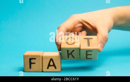 Ein Mann stellt Holzblöcke mit den Worten Fakt und Fake. Konzept von Nachrichten und falschen Informationen. Gelb drücken. Stockfoto