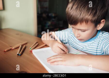 Niedlicher Junge sitzt am Schreibtisch und zeichnet in Album mit Buntstiften, Lifestyle Stockfoto