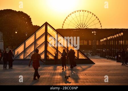 PARIS, FRANKREICH - 4. MAI 2018: Das Louvre Museum und ein großes Rad im Hintergrund, das beim Sonnenuntergang beleuchtet wird. Stockfoto