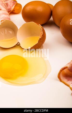 Zerbrochenes Hühnerei, Hühnereier, Speckscheiben und Wurst und Tomaten auf weißem Hintergrund. Nahaufnahme Stockfoto