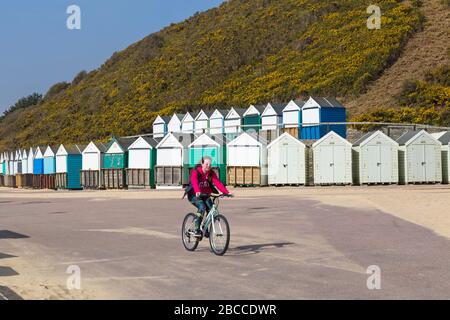 Bournemouth, Dorset UK. April 2020. Die Strände von Bournemouth sind hauptsächlich leer, außer denen, die die Küste besuchen, um ihre erlaubte Bewegung zu Unternehmen, da die Besucher rieten, zu Hause zu bleiben und sich an die Einschränkungen von Coronavirus für soziale Distanzierungen zu halten, wobei Parkplätze geschlossen sind, um Besucher aus der Ferne zu schrecken. Radfahrer fährt auf der Promenade vorbei an Strandhütten am Middle Chine - Frau mit dem Fahrrad. Credit: Carolyn Jenkins/Alamy Live News Stockfoto