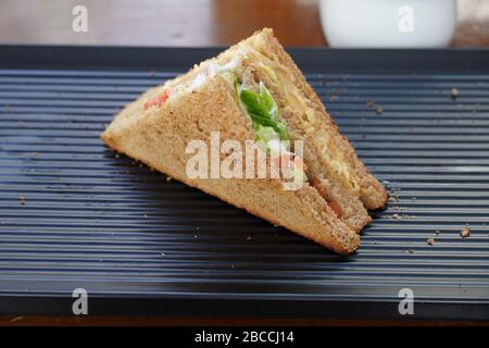 Ein einzelnes Thun-Sandwich auf schwarzem Servierblech. Ein Club Sandwich mit Huhn, Schinken, Käse, Tomaten, Gurke, Speck, Salat, Kräutern und geröstetem Brea Stockfoto