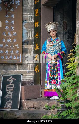 Feng Huang, China - August 2019: Schöne Chinesin in traditioneller Volkstracht gekleidet und posiert für ein Bild vor dem Eingang zum ol Stockfoto