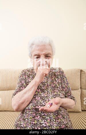 Eine ältere Frau, die Pillen hält, um ihr Husten zu stoppen. Weniger ist eines der Symptome für das kovid-19-Corona-Virus. Stockfoto