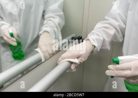 Frau, die mit feuchtem Wischtuch und alkoholhalmigem Desinfektionsspray das Geländer im Aufzug säubert. Desinfektion, Sauberkeit und Gesundheitsversorgung, Anti Coronavirus COVID Stockfoto