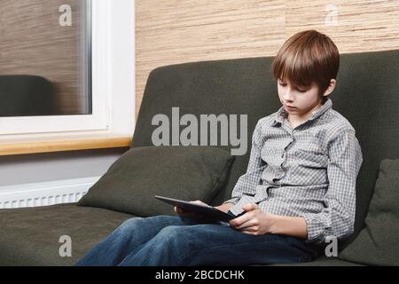Einsamer Junge, der auf dem Sofa sitzt und einen Tablet-Computer hat, der während der Isolation zu Hause festsitzt. Quarantäne und Sperrungen sind Schutzmaßnahmen gegen die Verbreitung von Co Stockfoto