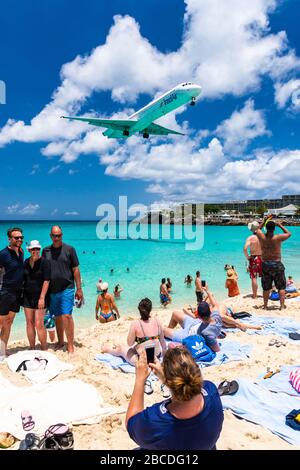Frau, die eine Familie am Maho Beach fotografiert, während ein McDonnell Douglas MD83-Flugzeug von Inselair über dem Kopf fliegt