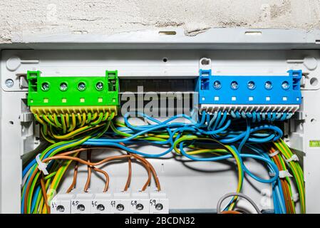 Grün-gelber und blauer Selbstklemmblock für elektrische Leitungen, montiert in der Elektrobox mit angeschlossenen Kabeln. Stockfoto