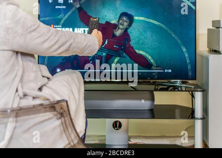 Netflix La Casa De Papel. Frau mit Multimedia-Fernbedienung in Handansicht auf TV Money Heist HIT-Serie. Stockfoto