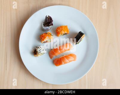 Sushi-Menü mit rohem Lachs, Reis und Tunarrolle auf einem Teller mit Holztischhintergrund. Japanische Küche. Draufsicht. Stockfoto