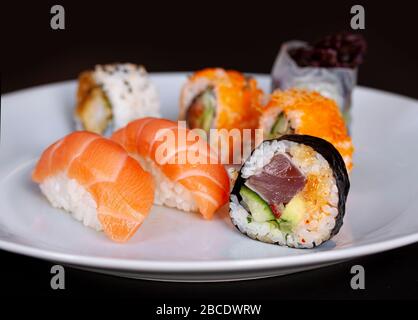Sushi-Menü mit Lachs, Reis und Thunfischrollen auf einem Teller mit schwarzem Hintergrund. Japanische Küche. Nahaufnahme mit selektivem Fokus. Stockfoto